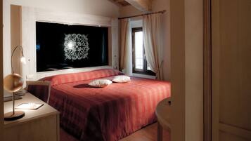 Un dormitorio con un ventanal grande, una cama con ropa de cama roja, una mesita de noche con una lámpara y una silla.