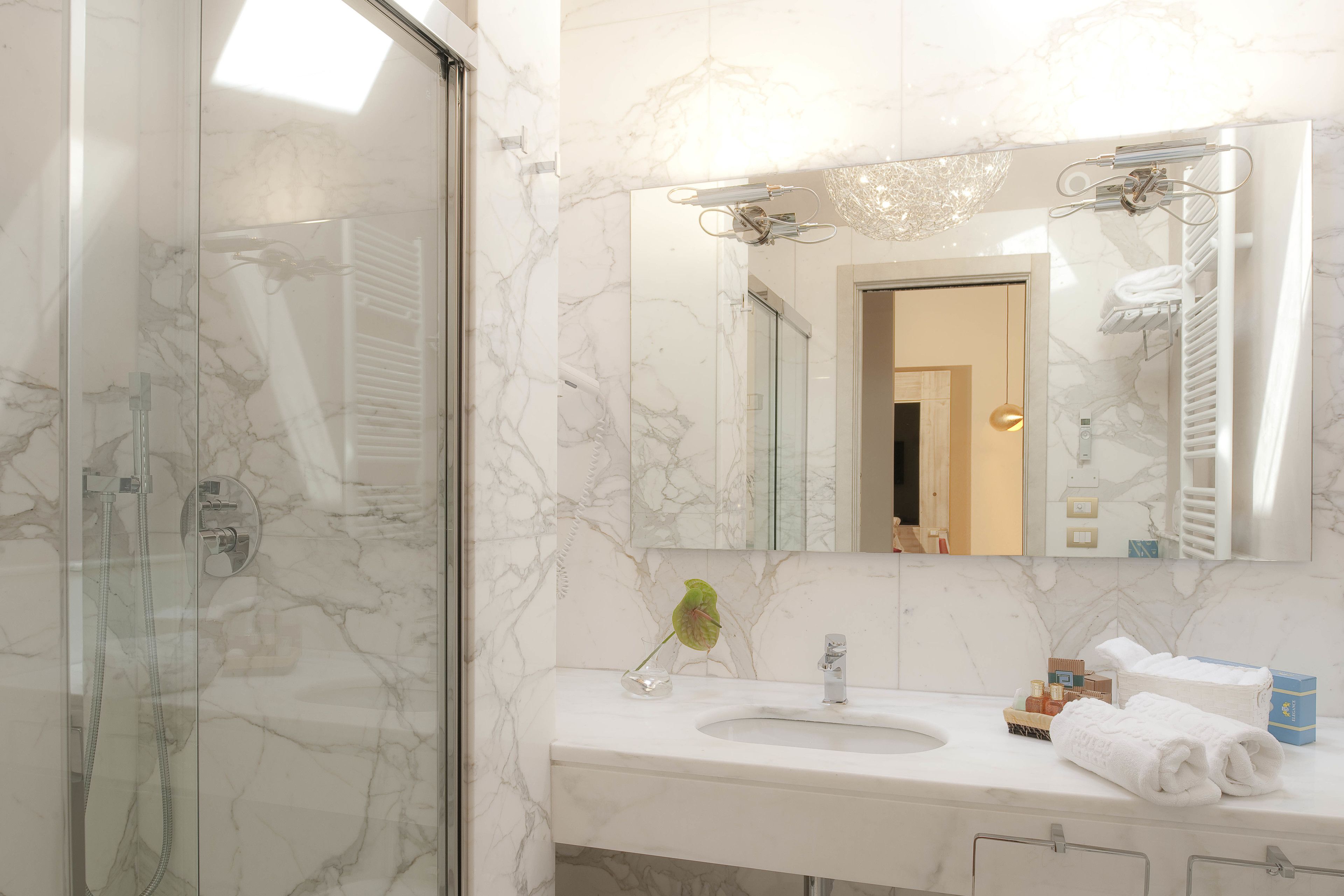 Un baño con cabina de ducha de vidrio, lavamanos de mármol y un espejo grande con toallero.
