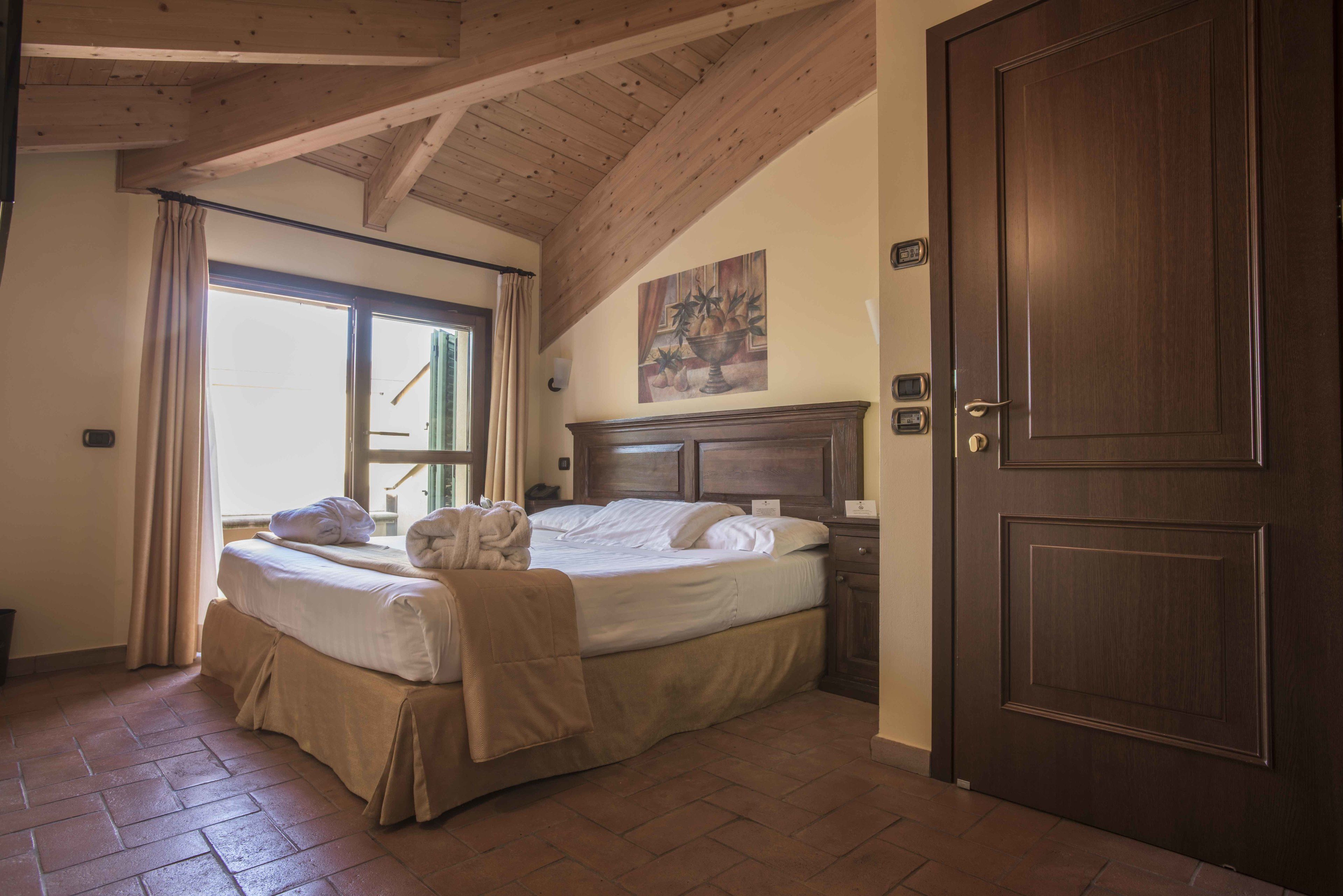 Une chambre à coucher avec un grand lit, des poutres apparentes en bois au plafond, une porte et une fenêtre avec des rideaux.