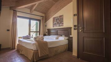 Une chambre à coucher avec un grand lit, des poutres apparentes en bois au plafond, une porte et une fenêtre avec des rideaux.