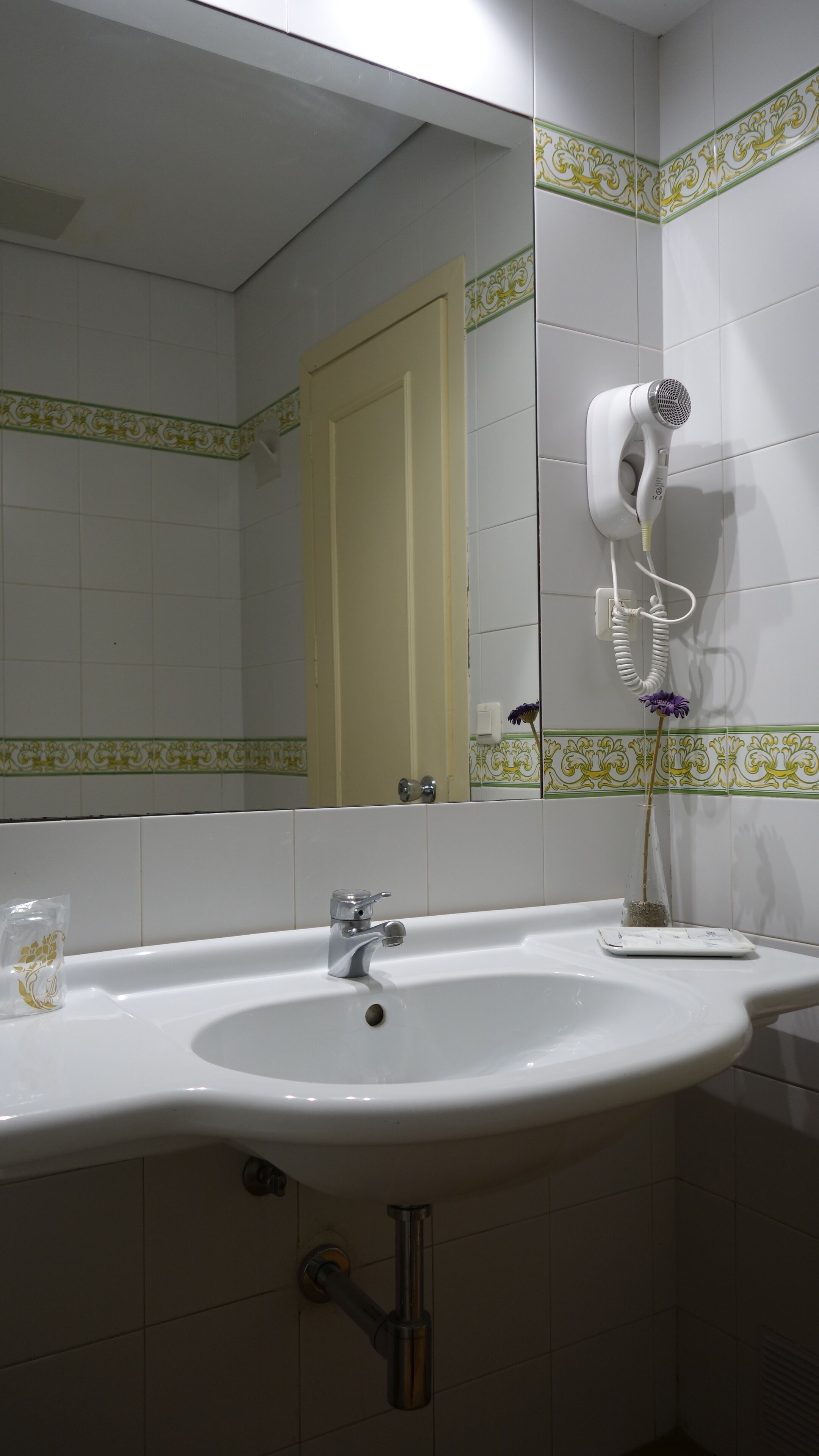 A bathroom with a sink, mirror, and hairdryer mounted on the wall.
