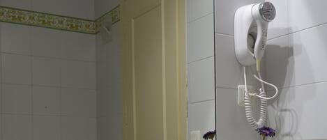 Casa de banho com lavatório, espelho e secador de cabelo fixado na parede.