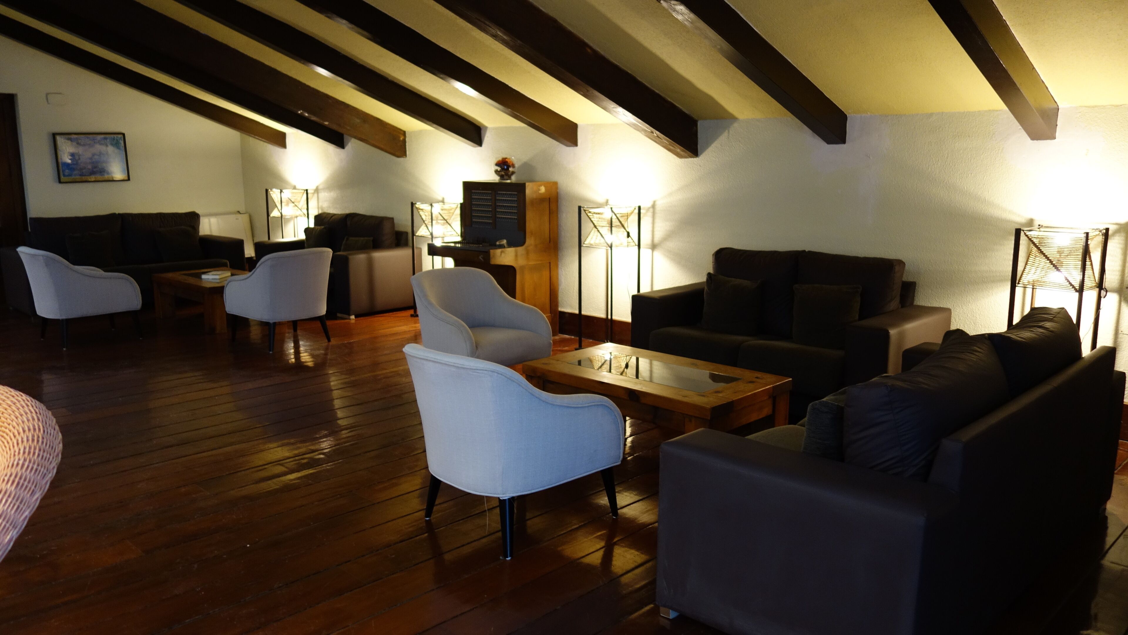 A spacious lounge area with wooden flooring, multiple seating options including sofas and armchairs, and a variety of lighting fixtures.
