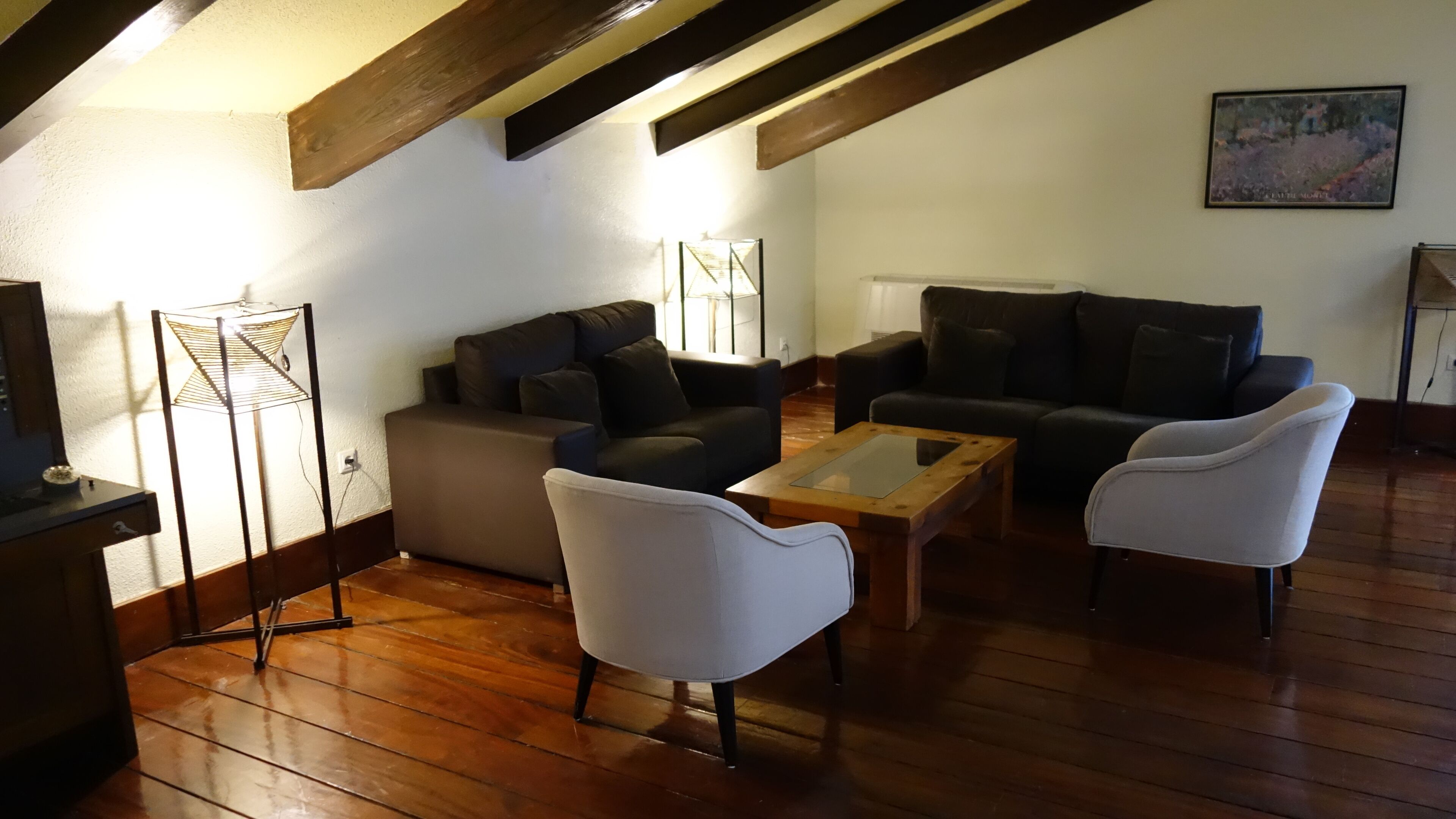 Un salon chaleureux avec un plancher en bois, un canapé, deux fauteuils et une table basse. Un tableau est accroché au mur et une lampe se trouve sur un pied.