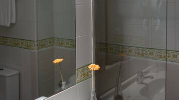 Een badkamer met een wit wastafel, een spiegel, een douche en een vaas met een bloem.