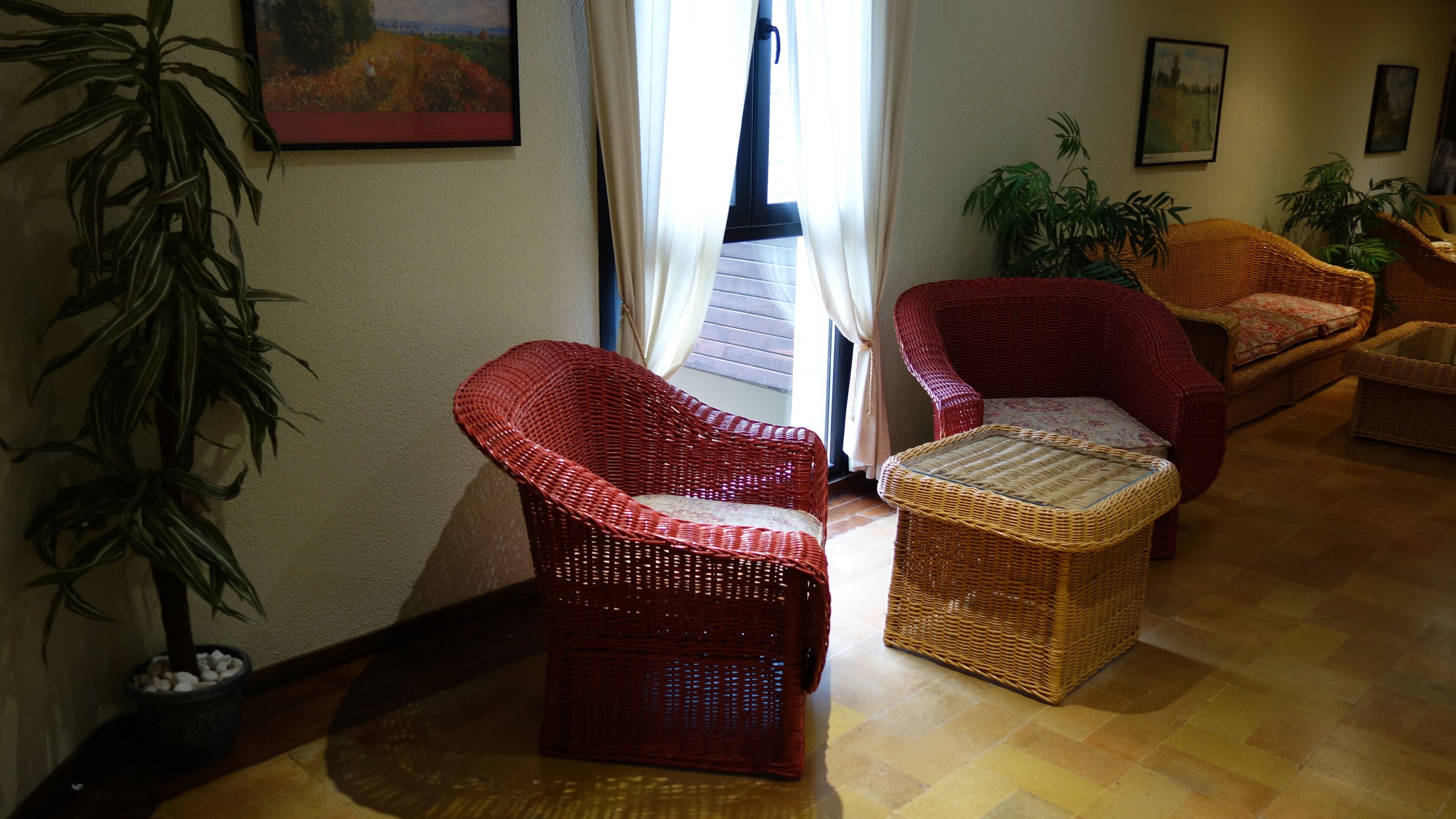 A living room with wicker furniture, a potted plant, and a painting on the wall.