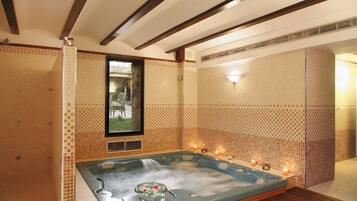 A spa room with a hot tub, wooden beams, tiled walls, and candles.