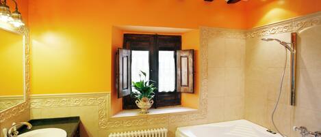 Un baño con bañera, una ventana con contraventanas y un radiador.