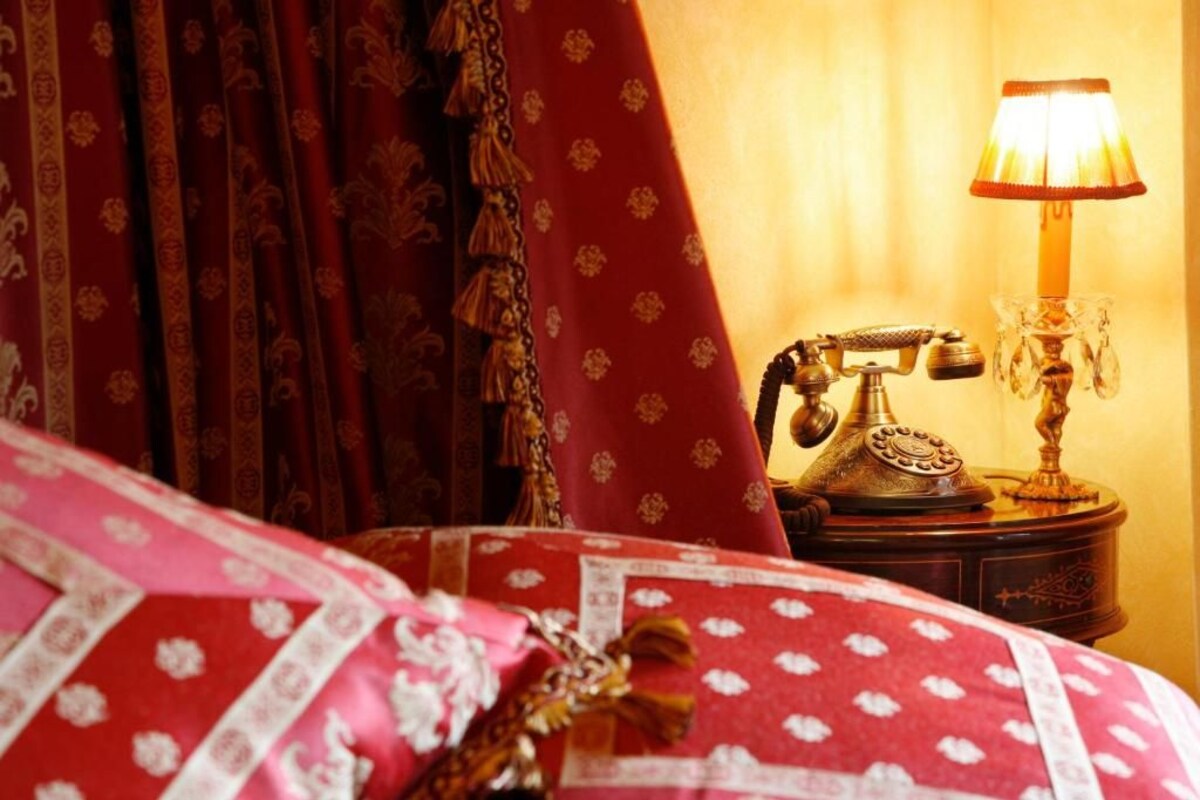 A bed with a red and white patterned bedspread, a brass telephone on a wooden nightstand, and a lit table lamp.