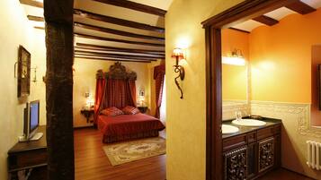 A bedroom with a wooden floor, a bed with red bedding, a nightstand with a lamp, and a large mirror above a sink.