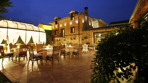 An outdoor patio with tables and chairs, a brick building in the background, and a tent on the left.