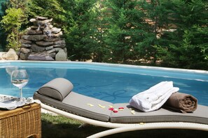 A poolside lounge chair with a towel and a glass of wine, a stone waterfall, and a lush green backdrop. - Hotel Boutique Real Casona de las Amas (Azofra)