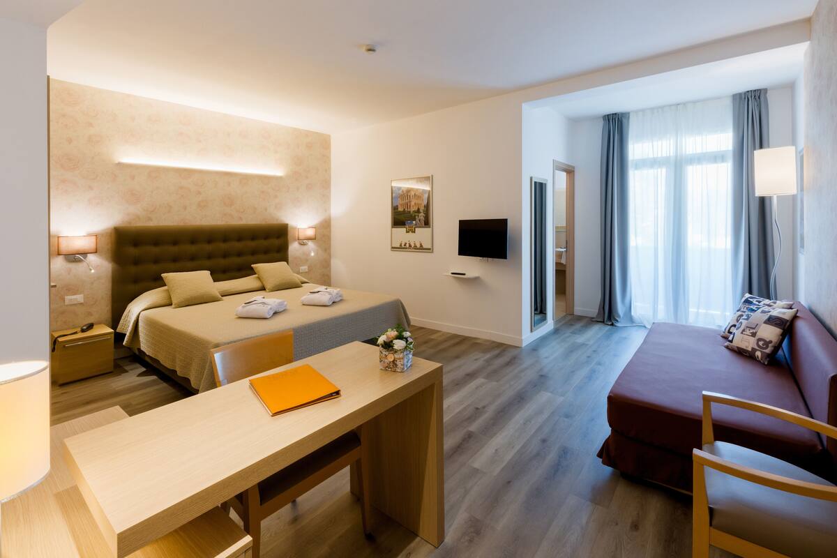 Une chambre d’hôtel équipée d’un lit, d’un bureau, d’une chaise, d’un canapé et d’une télévision.