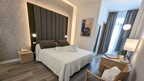 Ein modernes Hotelzimmer mit einem großen Bett, einem Nachttisch, einem Sessel und einem Schreibtisch mit einer Lampe.