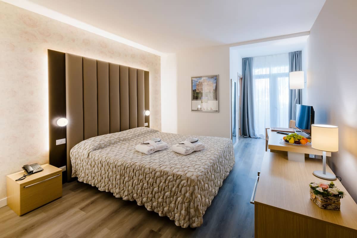 Une chambre d’hôtel moderne avec un grand lit, une table de chevet, une lampe et une vue sur la ville par la fenêtre.