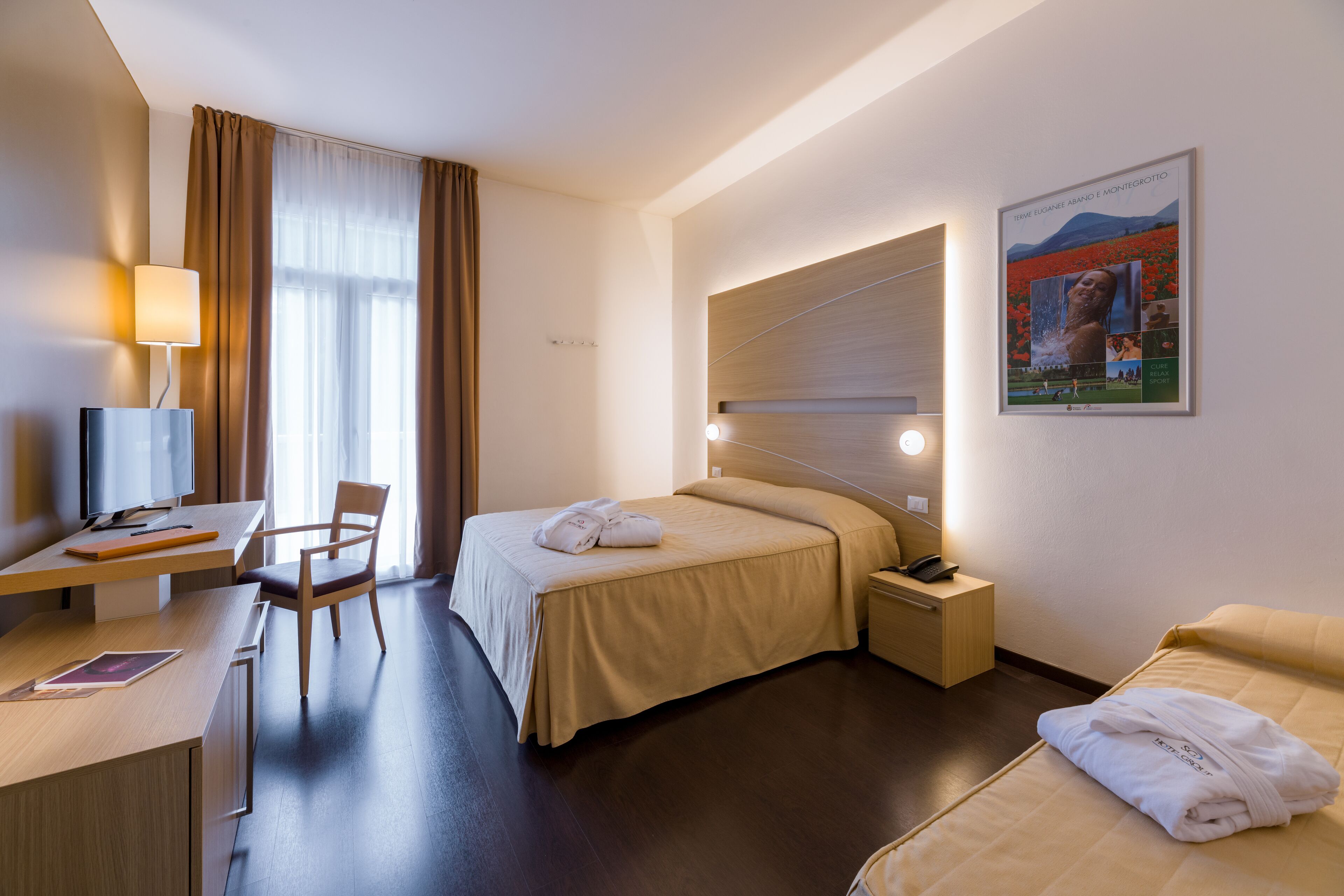 Camera d'albergo con un letto, una scrivania, una sedia, un comodino e una TV a parete.