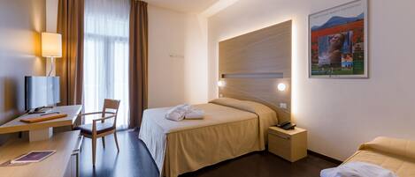 Ein Hotelzimmer mit Bett, Schreibtisch, Stuhl, Nachttisch und einem an der Wand befestigten Fernseher.