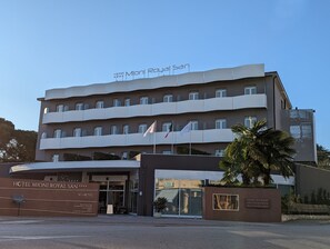 Un hôtel à plusieurs étages doté de balcons, une enseigne indiquant « Hôtel Mioni Royal San » et une enseigne indiquant un complexe thermal.