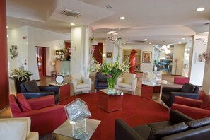 Un hall d’hôtel moderne avec des canapés en cuir, une table basse centrale et un vase décoratif rempli de fleurs.
