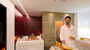Ein Spa-Raum mit einer Badewanne, einem Tisch mit einer Obstplatte und Getränken, und einer Person, die Speisen serviert.