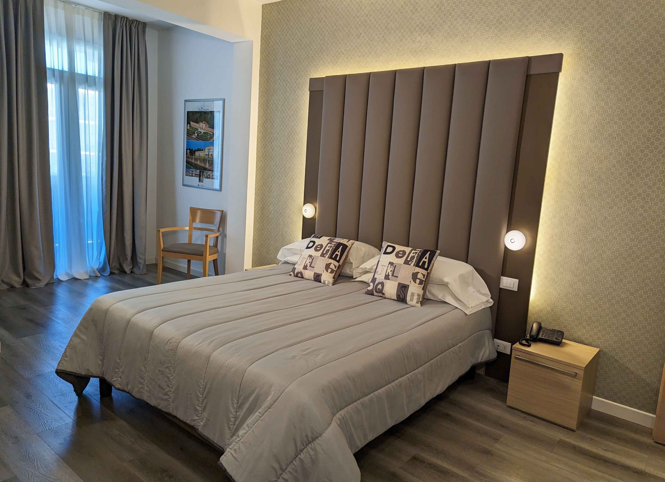 Un cuarto de hotel ordenado con una cama grande, una mesita de noche con un teléfono y una silla.