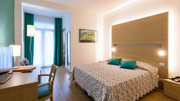 Una habitación de hotel con cama, escritorio, silla y un cuadro en la pared.