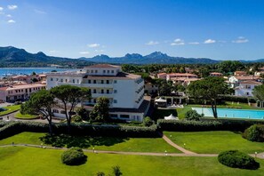 A coastal hotel with multiple buildings, a swimming pool, and a mountainous backdrop. - Hotel Baja  (Arzachena)