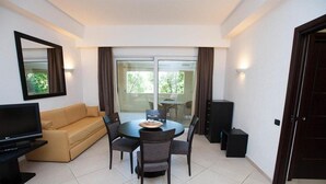 A modern living room with a sofa, TV, dining table, and chairs. - Hotel Baja  (Arzachena)