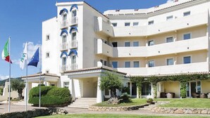 A multi-story hotel with a white facade, balconies, and a covered outdoor area with greenery. - Hotel Baja  (Arzachena)