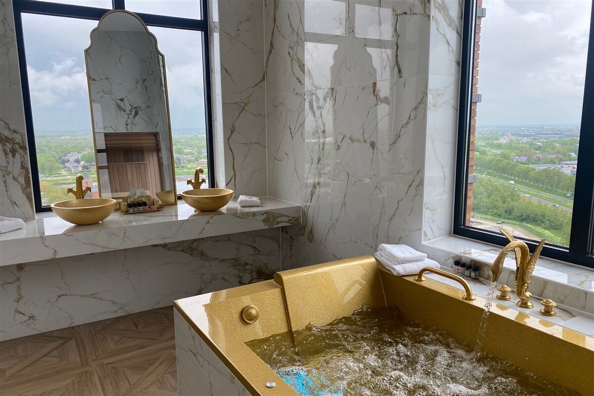 A bathroom with a bathtub, a sink with a marble countertop, and a large window offering a view of a green landscape.