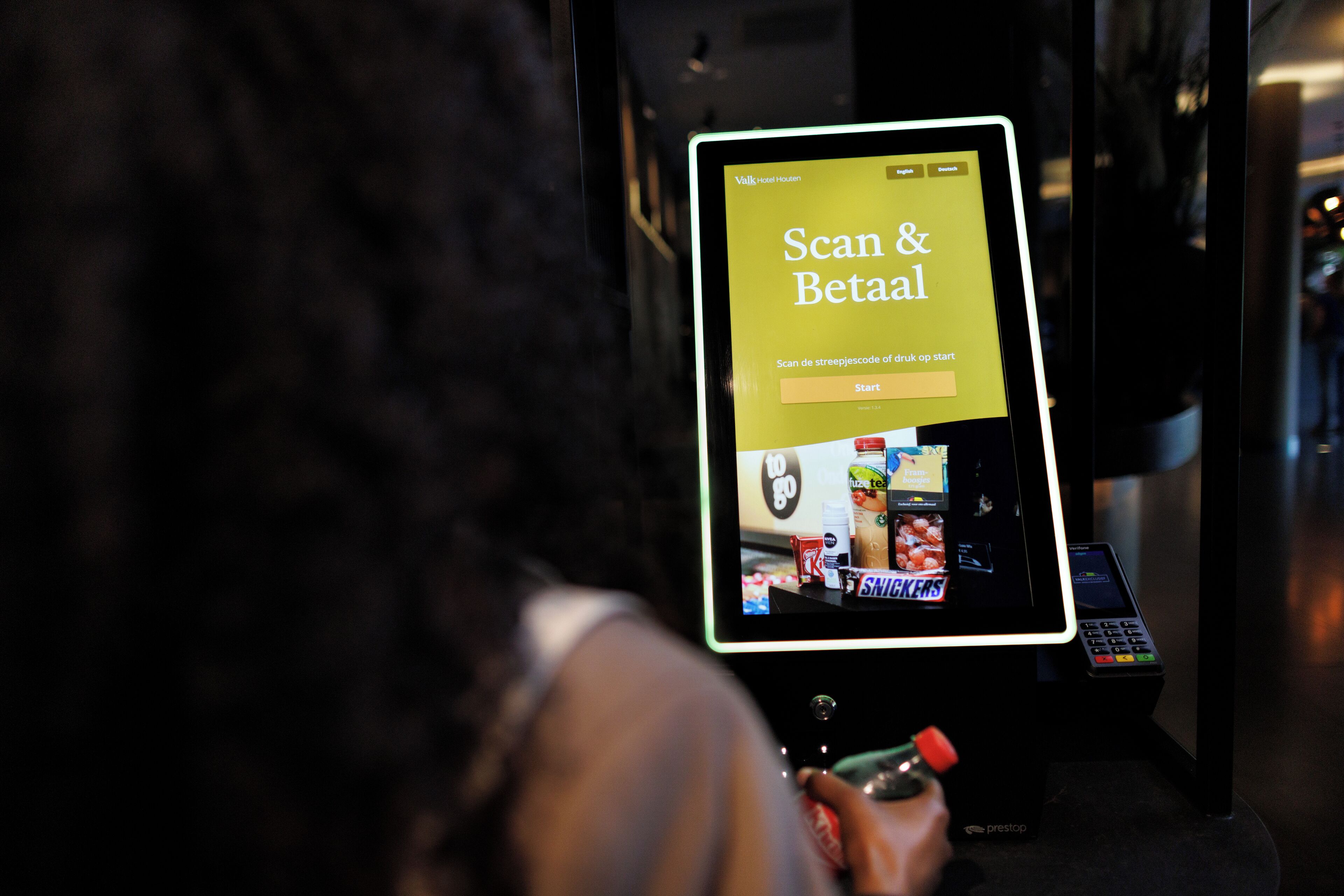 Un quiosc digital amb una pantalla que mostra una interfície "Scan & Betal" per a un servei d'hotel.
