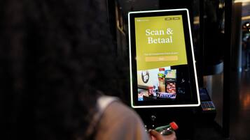 Un quiosc digital amb una pantalla que mostra una interfície "Scan & Betal" per a un servei d'hotel.