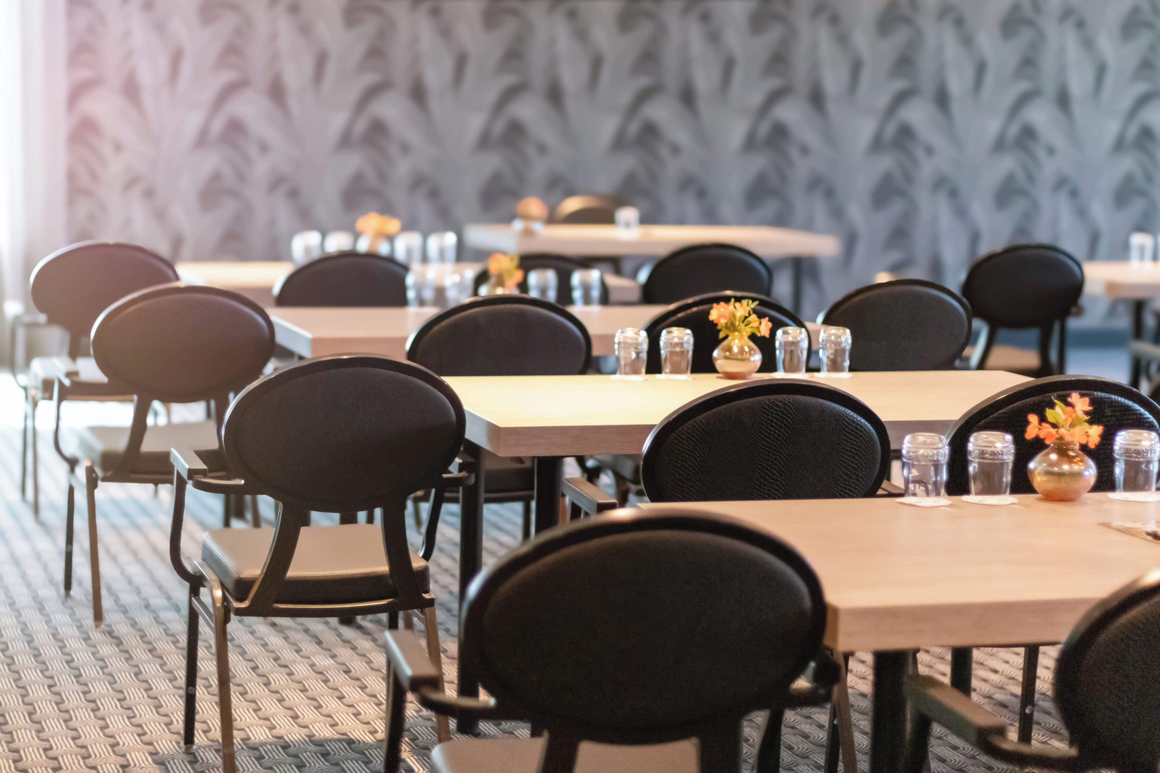 A conference room with multiple tables and chairs, arranged in rows.