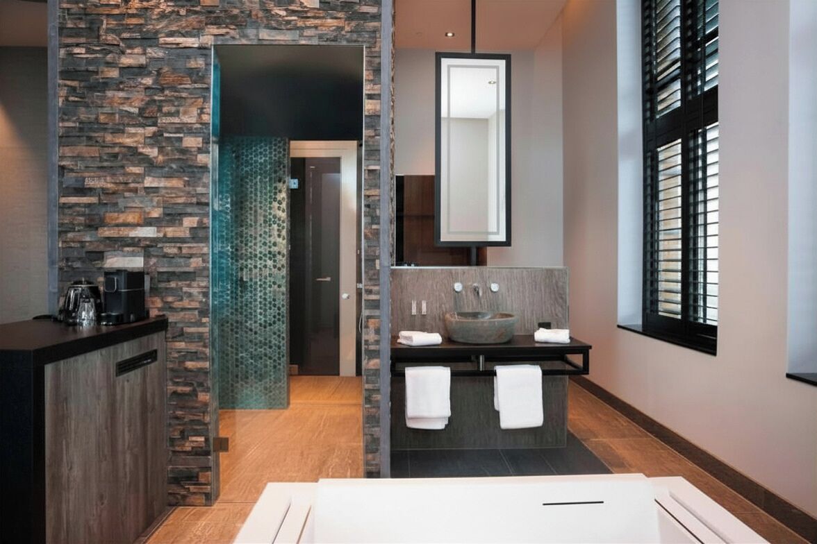 A modern bathroom with a stone wall, a large mirror, a sink with a vessel basin, and a coffee machine on the counter.