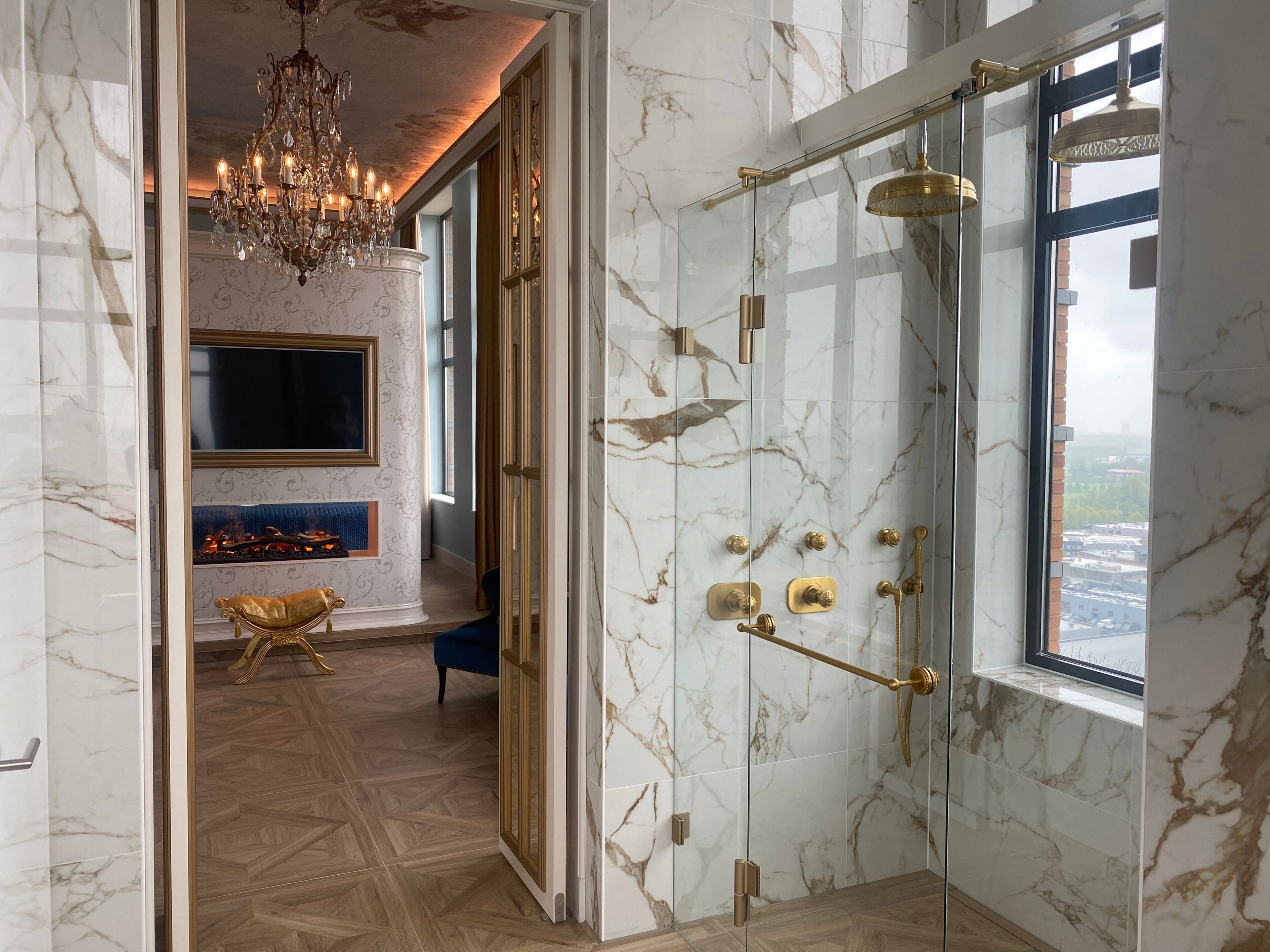 Een luxe badkamer met een douchecabine van glas, marmeren wanden en een kroonluchter.