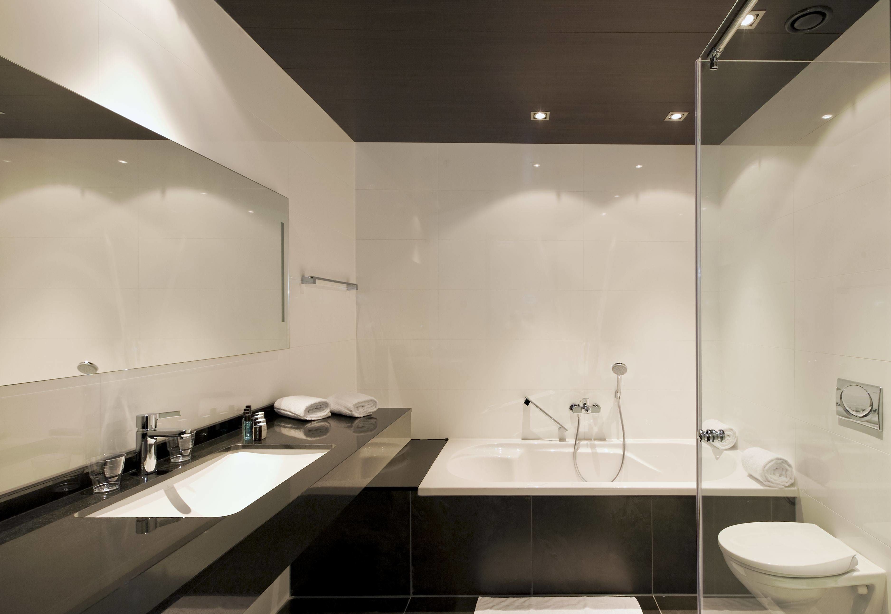 Un baño moderno con un espejo grande, una encimera negra, un lavamanos blanco, una bañera y un inodoro.
