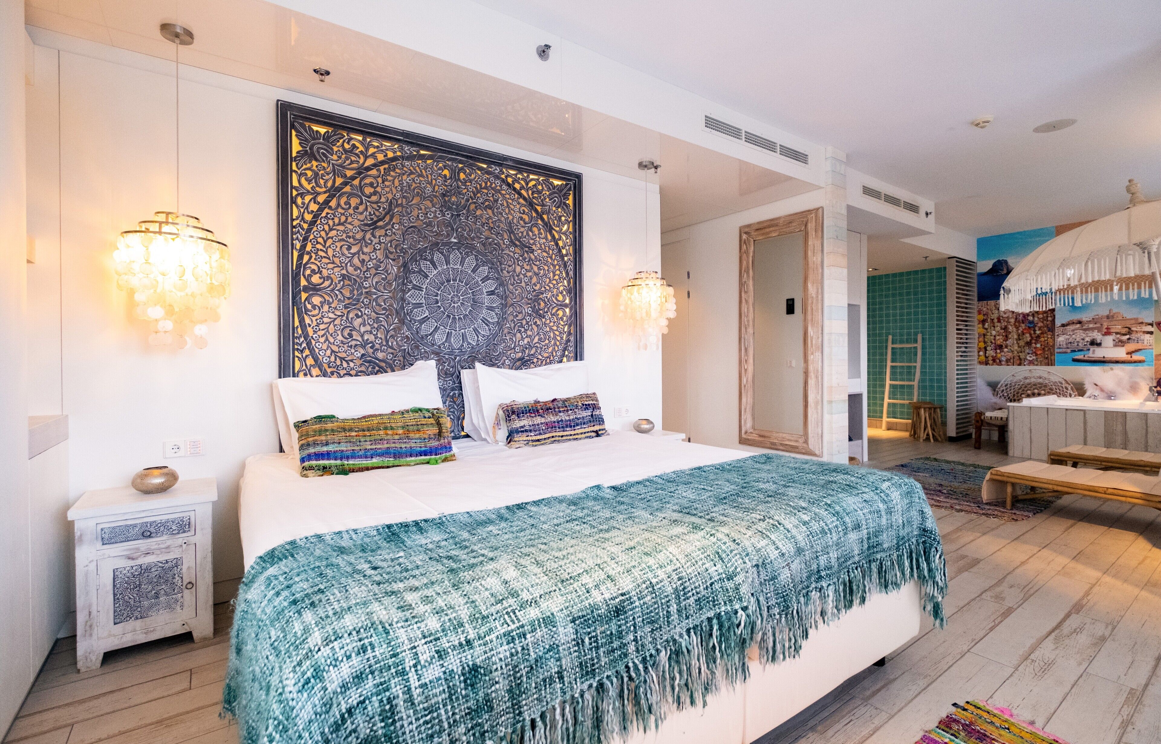 A modern bedroom with a large bed, decorative wall panel, two bedside lamps, and a view of the bathroom.