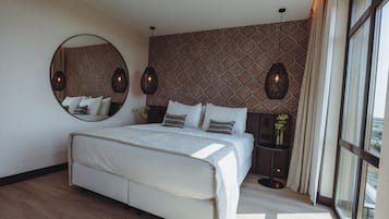 A modern bedroom with a large bed, a round mirror, patterned wallpaper, and pendant lighting.