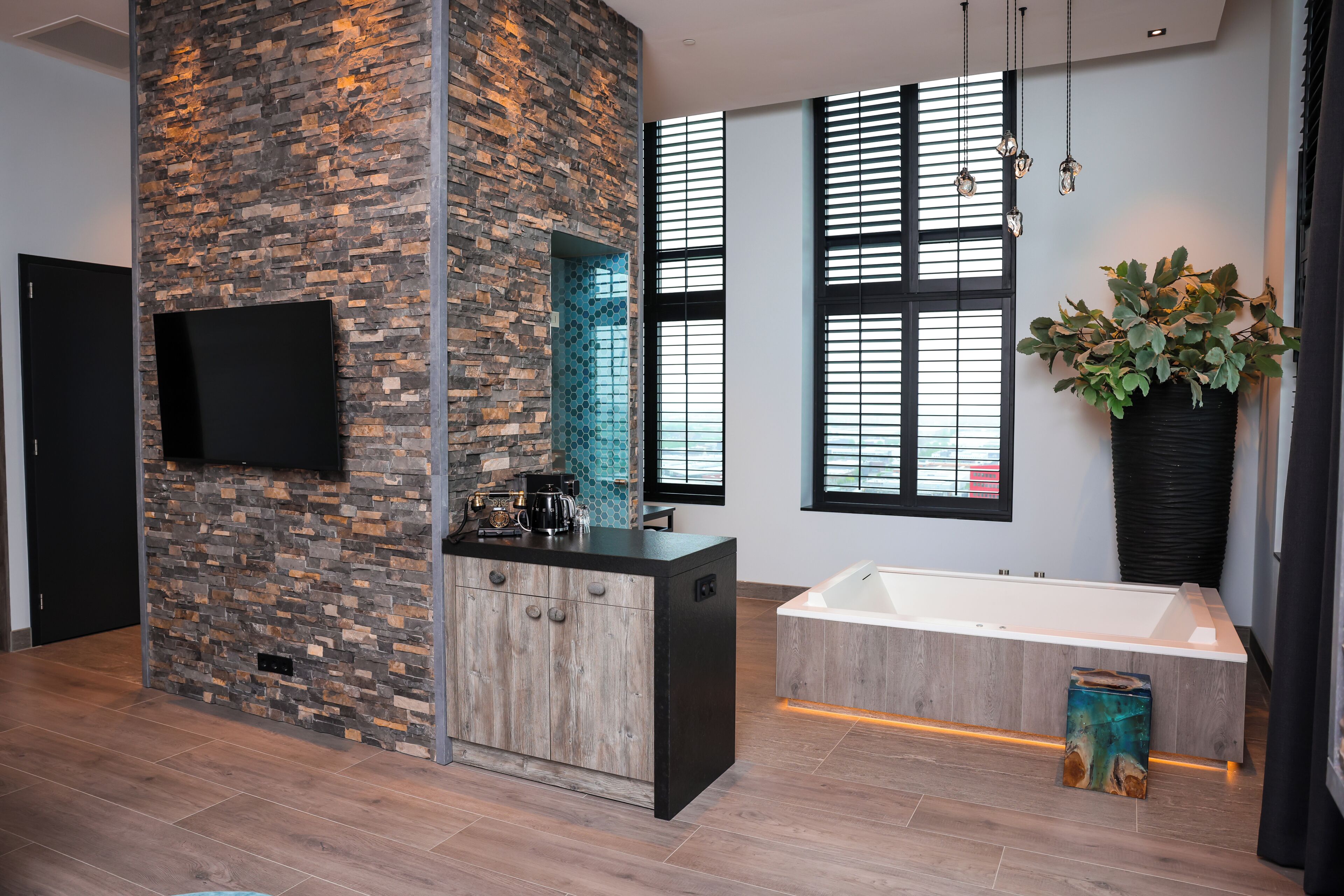 Un baño moderno con una pared decorativa de piedra, una bañera independiente y una planta grande en maceta.