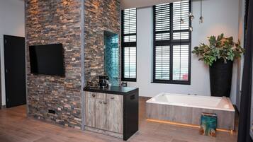 Une salle de bain moderne avec un mur d’accent en pierre, une baignoire sur pieds et une grande plante en pot.