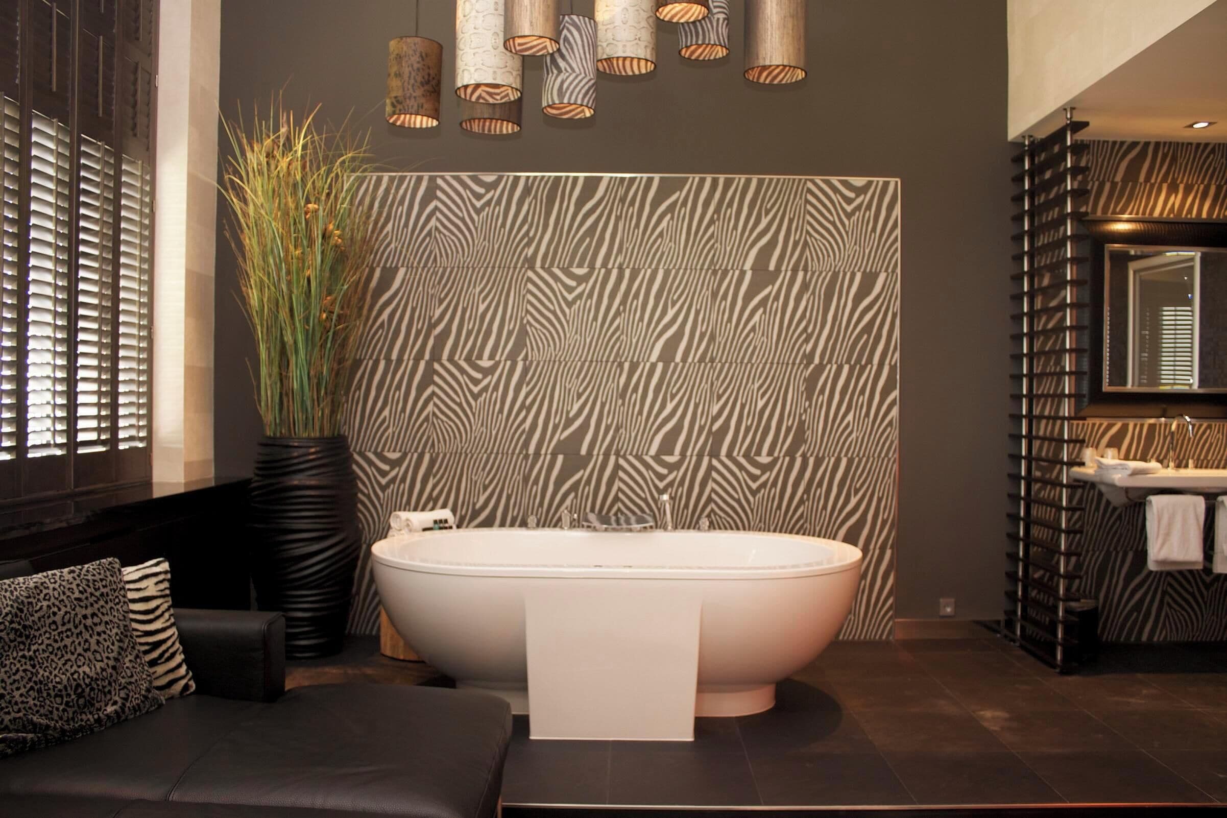 Een moderne badkamer met een vrijstaand bad, een muur met zebrapatroon en een grote spiegel boven de wasbak.