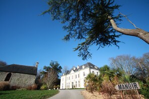 A large, historic building with a prominent entrance, surrounded by lush greenery and a clear blue sky. - Manoir des Indes, The Originals Relais (Quimper)
