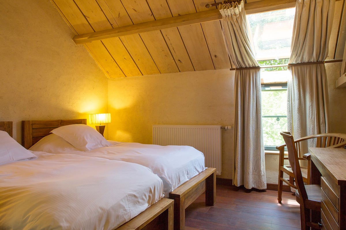 A room with two beds, a wooden bench, a table, and a window with curtains.