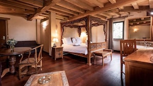 Una cama tradicional con dosel de madera, un mesita de noche con lámpara, una mesa redonda de madera con sillas, y un banco de madera.