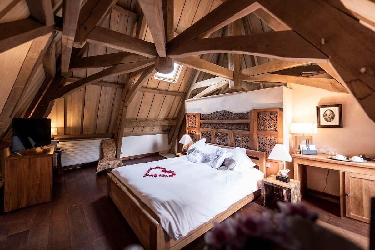 A bedroom with a sloped ceiling, a bed, a desk, and a chair.