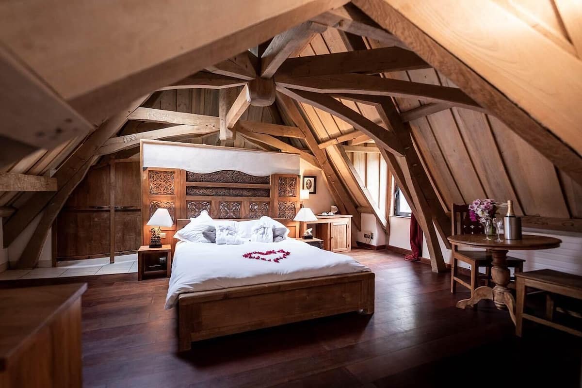 A cozy attic bedroom with a wooden bed, nightstands, and a small table with a vase of flowers.