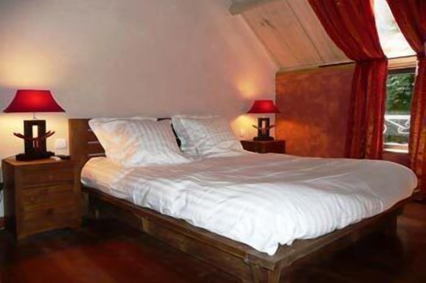 Un dormitorio con una cama de madera, dos mesitas de noche y lámparas rojas.