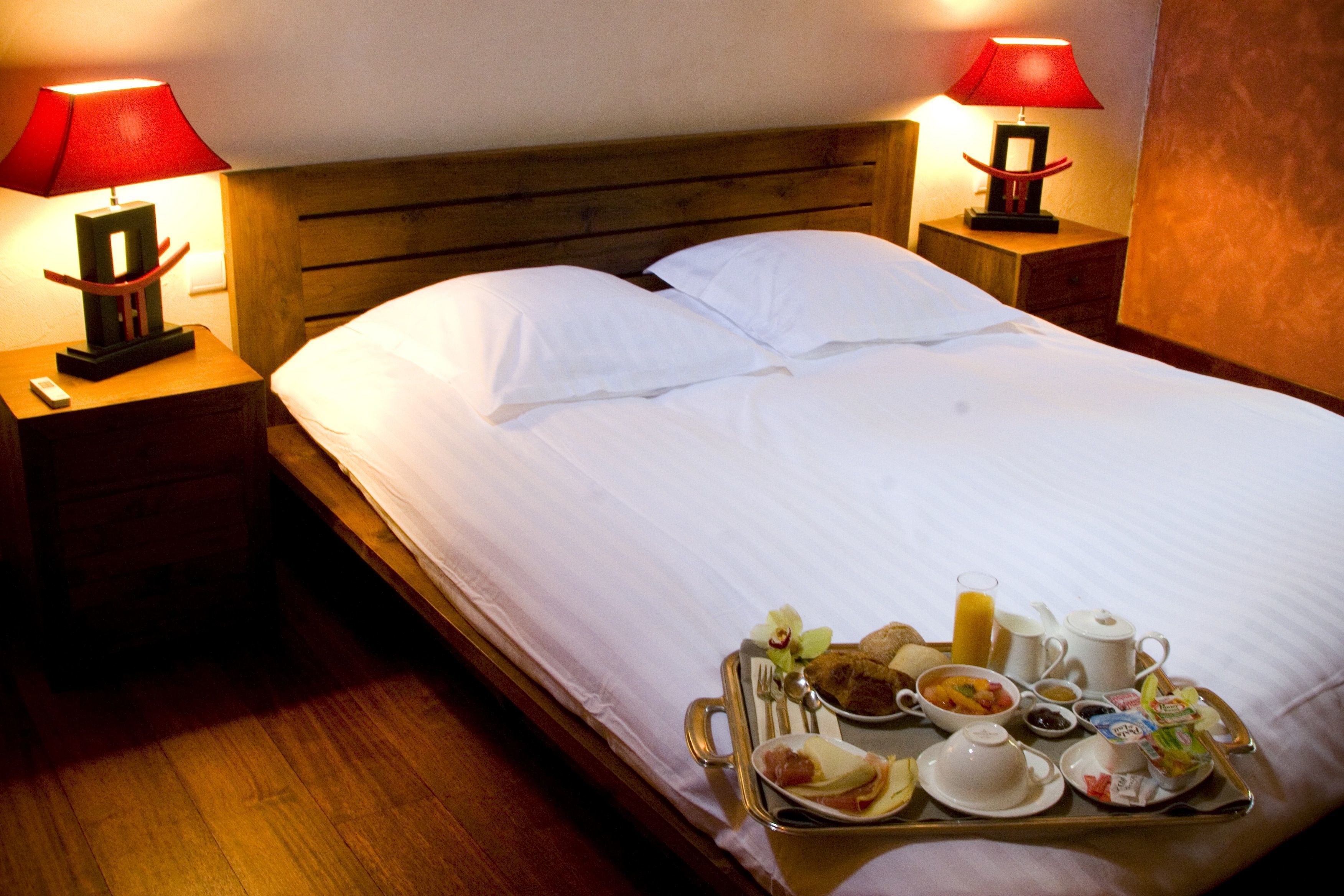 Habitación de hotel con una cama bien hecha, dos mesitas de noche con lámparas y una bandeja con alimentos para el desayuno sobre la cama.