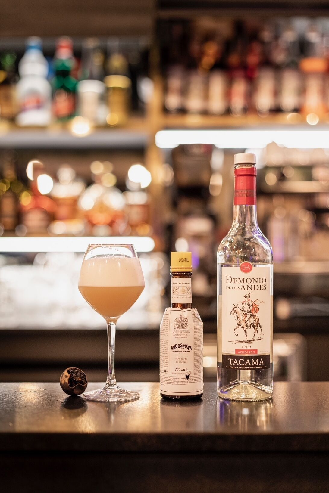 Un bar avec une bouteille de pisco Demonio de los Andes Tacaima, une bouteille d’amer Angostura et un verre de cocktail.