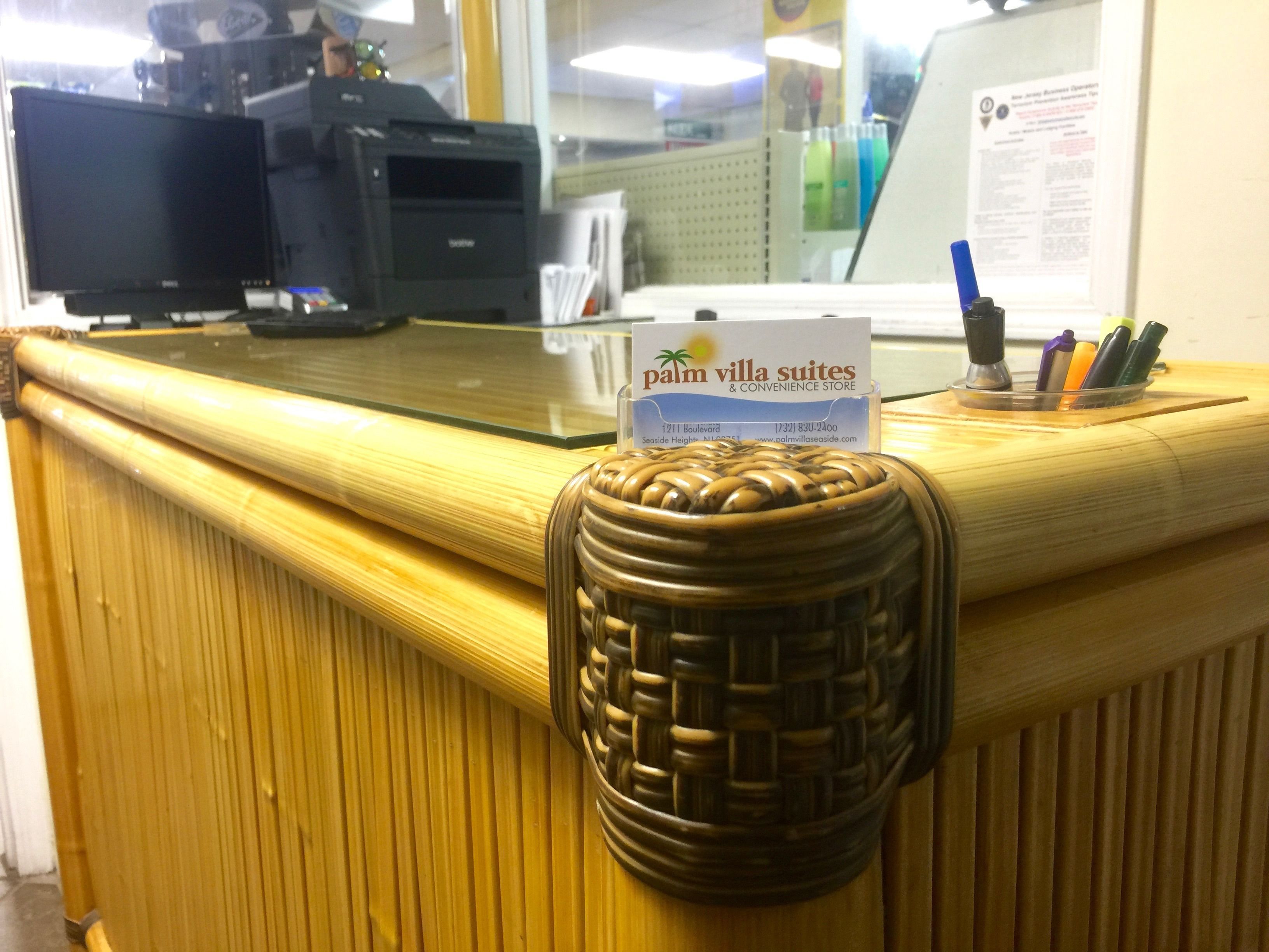 A reception desk with a sign for Palm Villa Suites & Convenience Store, a computer, and a pen holder with pens.